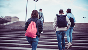 Teenagers outside walking up stairs with backpacks to school